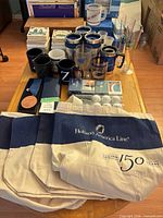 Lot overview on table showing tote bags, mugs, tumblers, glasses, coasters, medals, golf balls