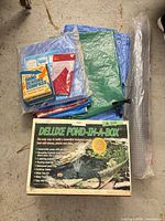 Stacked items: pond kit box, tarps, compass package, mesh roll