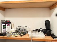 Full shelf view with camera, cover, chargers, cables, storage case, phone handset box, calculator, recorder