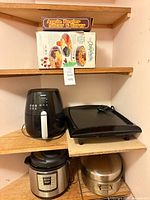 Shelf view showing boxed apple peeler, boxed dehydrator, Philips air fryer, electric griddle, Instant Pot and roasting pan
