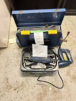 Open blue carry case holding rotary tool, accessories, and manual; jigsaw alongside