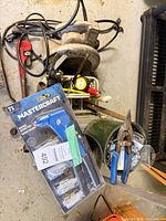 Mixed tools on floor: packaged Mastercraft riveter, bench grinder, tin snips, tape measure, fastener container