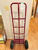 Full view of red hand truck leaning against wall