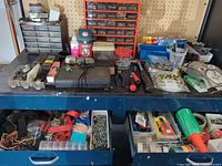 Workbench top with small parts drawer cabinets, hand tools, fasteners, adhesives and storage bins visible