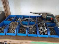 Blue plastic bins containing assorted screws, bolts, nuts, washers, steel wire rope coil and corded electric drill