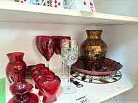 Shelf with red wine glasses, hand-painted glass, mosaic vase, platters