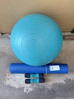 Top view of teal stability ball, rolled blue yoga mat, pair of foam dumbbells