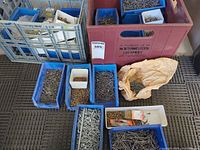 Multiple blue bins and paper bag of assorted nails and screws on floor next to grey crate