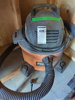 Full view of Ridgid wet/dry vacuum showing orange drum, black motor top, handle, hose and cord