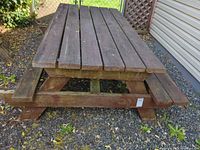 Overall view of wooden picnic table with two attached benches on gravel surface
