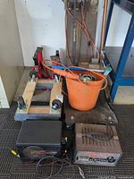Two battery chargers, dolly, bucket of tools, jack stands in background