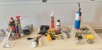 Full layout of assorted tools, adhesives, WD-40, propane, tape measures on table