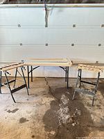 Two folding work stands with paint-splattered wooden tops beside a folding table (table not included)