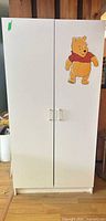 Front view of closed white two-door wardrobe with Pooh decal and metal handles