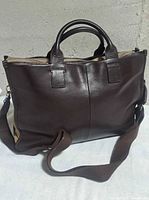 Front view of brown leather messenger bag with handles and strap