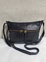 Front view showing pebbled leather, two zip pockets, strap