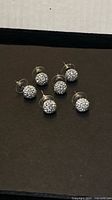 Three pairs of silvertone crystal stud earrings on black background