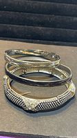 three stacked silvertone bangles showing designs