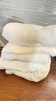 Stack of four white plush bath towels on wood floor