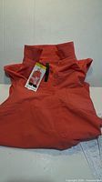 Front view of coral-orange Gaiam sleeveless button-front collared tank top with tags attached