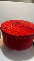 Closed red velvet hat box showing lid and cord handle