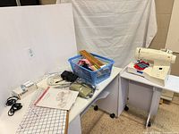 Overall lot showing sewing machine on rolling table, basket of notions, cords, manuals, fabric and accessories
