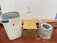 Front view Keenpure air purifier, TCL boxed filter, sealed spare filter, wood planks behind