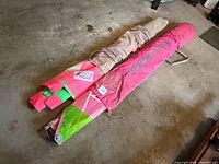 Both windsurf sails rolled in their carry bags lying on floor (pink Neil Pryde Slalom Lite; beige Alpha)