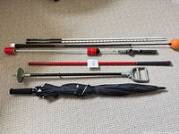 All six golf training and accessory items laid out on floor: two alignment sticks, speed trainer, Orange Whip, cane seat, folded umbrella