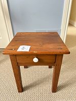 Full view of wooden side table showing top, legs, drawer with white knob
