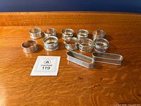 All twelve sterling silver napkin rings grouped on wooden surface