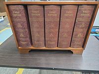 Front view showing five faux book spines labeled First Edition Adams