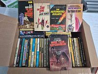 Open box showing assorted vintage sci-fi paperbacks with five titles displayed on top