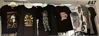 Six black graphic T-shirts hanging on hangers, showing front graphics and condition