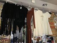 Five garments hanging: black fringe skirt, black bodysuit, rust ribbed dress, white dress, multicolor patterned dress