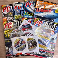Stack of PC Pilot magazines with several paper-sleeved CDs on wooden surface
