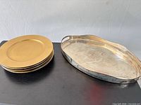 Stack of six gold charger plates next to oval silver tray