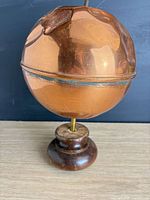 Front view of copper sphere on wooden pedestal displaying overall form and patina
