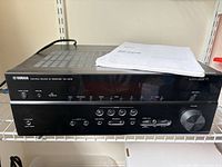 Front view of Yamaha RX-V675 receiver on shelf with manual on top