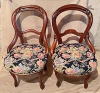Front view of both balloon-back chairs displaying wood frames and floral seats