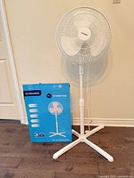 Assembled white Pelonis pedestal fan beside original box