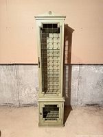 Front view of tall sage green curio cabinet showing metal grille door and lower compartment