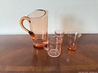 front view of pitcher, measuring cup and three tumblers on wood surface