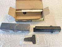 Box opened showing door closer body, plastic-wrapped cover, mounting bracket in bag