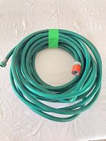 Coiled green reinforced vinyl garden hose with metal threaded fitting and orange quick-connect coupler