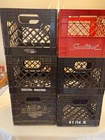 Stack of six plastic milk crates: five black Lactalis/Lactam and one red Sealtest