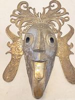 Front view of mixed metal mask showing filigree crest, side panels, facial features and patina