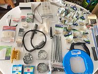 Overview of mixed lot showing packaged brass fittings, electrical boxes, blue fish tape reel and other hardware