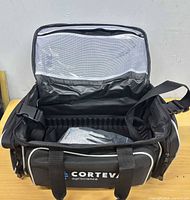 Open view of Corteva Agriscience tackle bag showing logo, interior, and included gloves