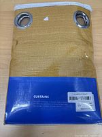 Front of sealed package showing mustard fabric with two metal grommets